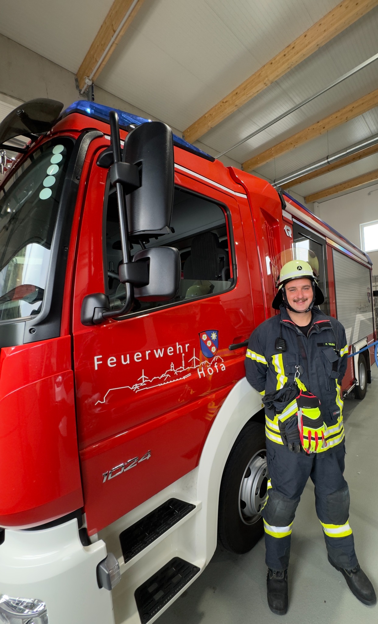 Patrick com uniforme de bombeiro ao lado de um veículo dos bombeiros de Höfa.